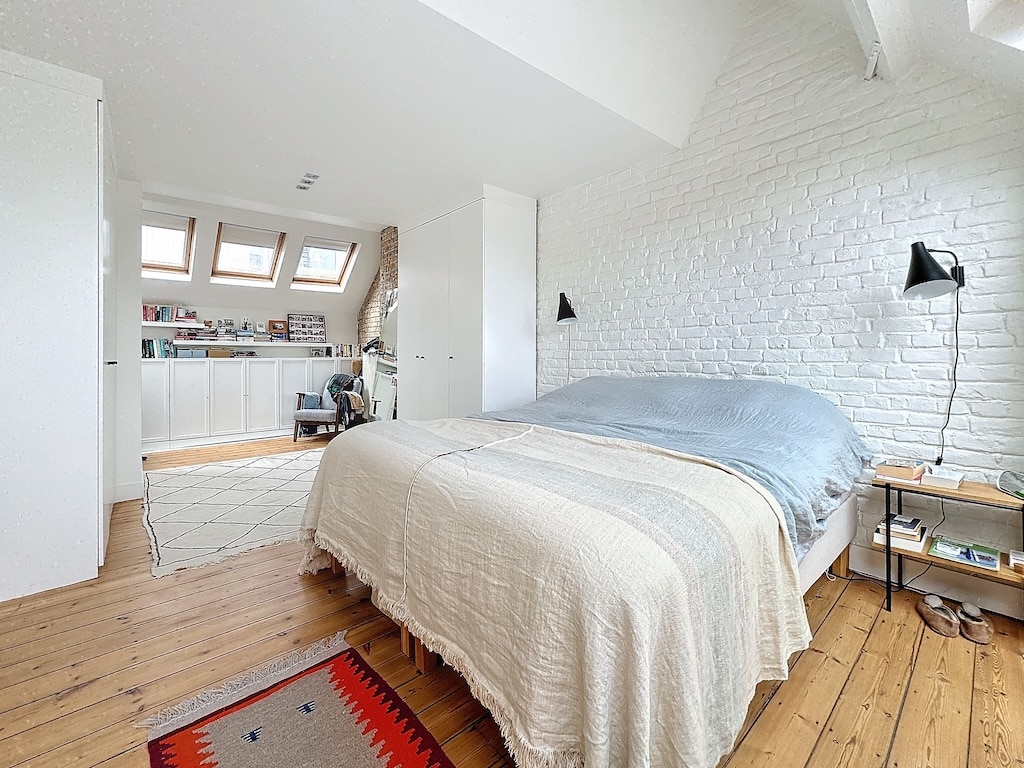 Chambre moderne et lumineuse avec lit, parquet clair, éclairage doux, ouverte sur cuisine blanche.