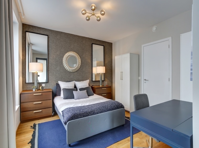 Chambre moderne élégante avec lit blanc, espace de travail, miroirs et ambiance chaleureuse.