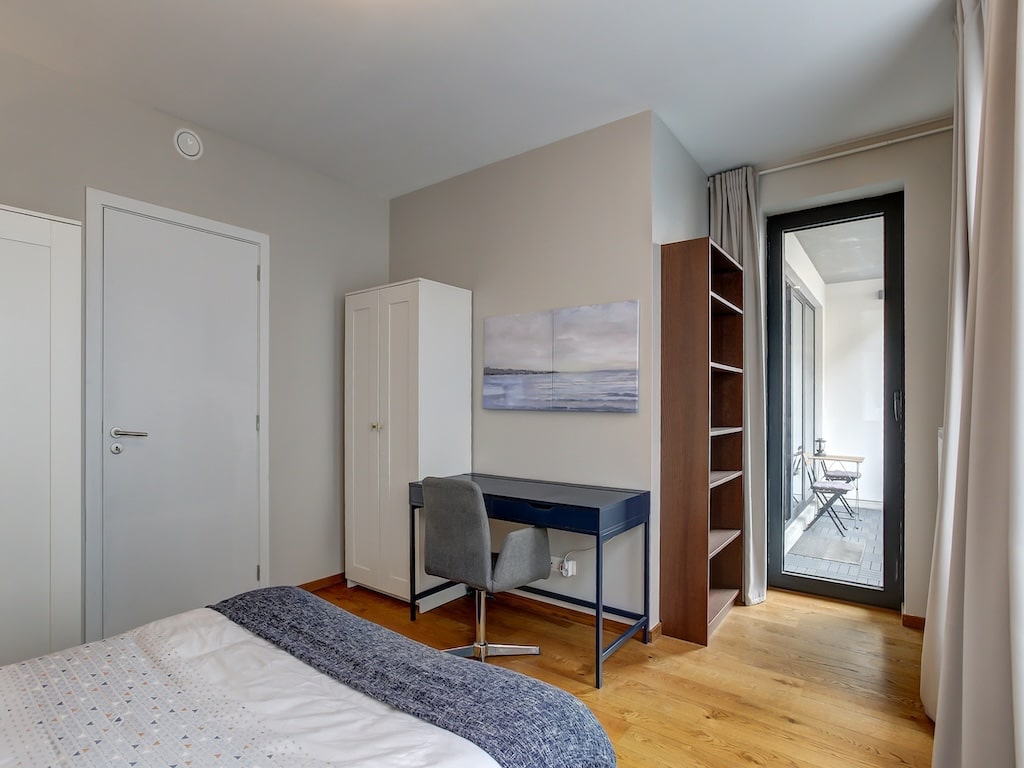 Chambre moderne lumineuse avec lit blanc, bureau minimaliste, vue sur balcon ensoleillé et décoration apaisante.