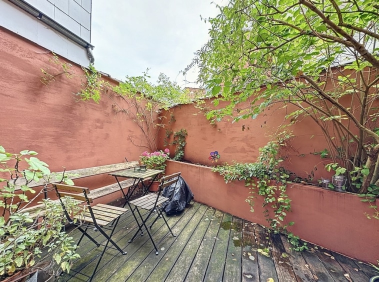 Coin jardin cosy avec plantes, mobilier rustique et murs couleur pêche pour moments de détente.