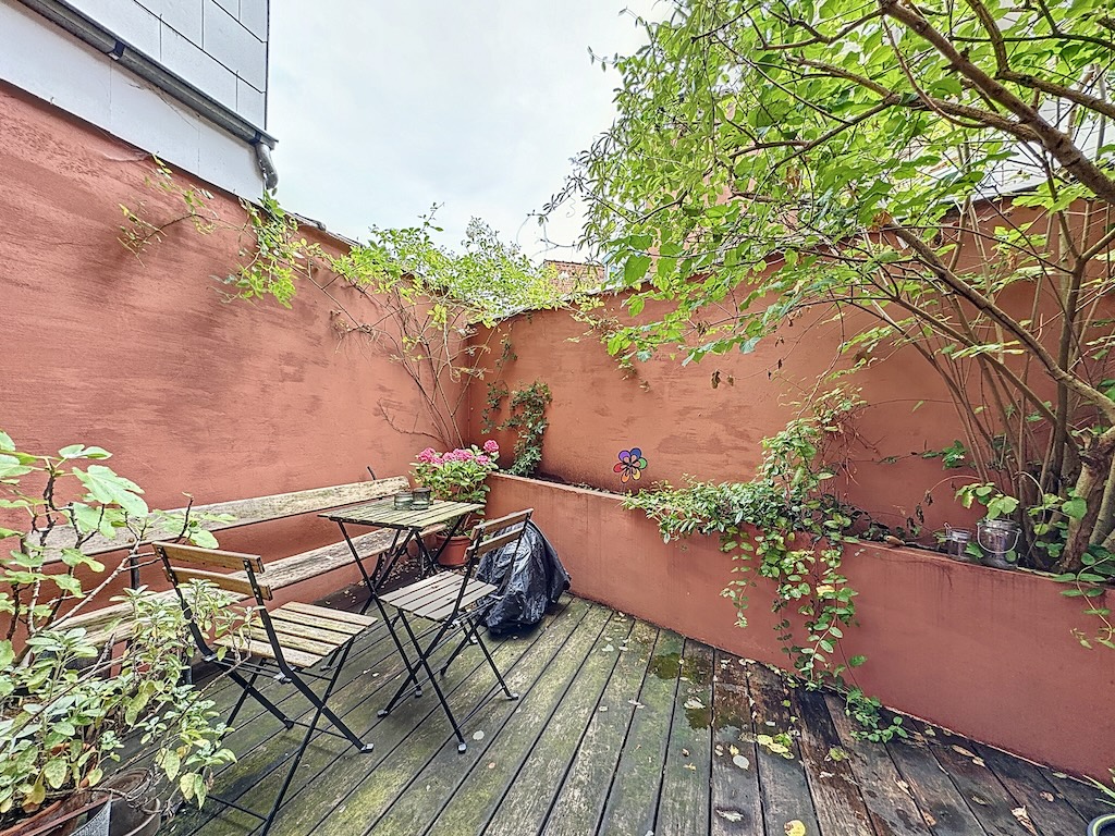 Coin jardin cosy avec plantes, mobilier rustique et murs couleur pêche pour moments de détente.