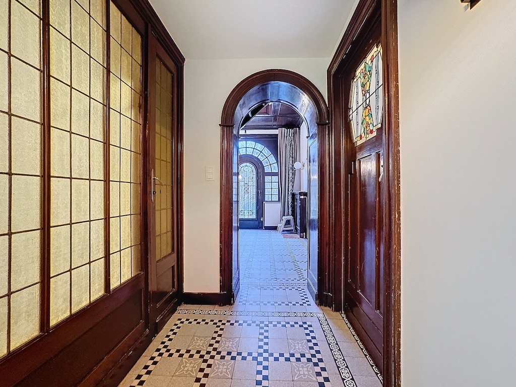 Couloir élégant en bois, carrelage noir et blanc, vitraux colorés, arches raffinées, ambiance sophistiquée.