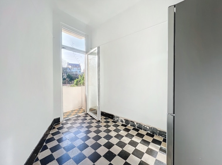 Cuisine lumineuse avec carrelage noir et blanc, grand fenêtre, réfrigérateur moderne, vue extérieure verdoyante.