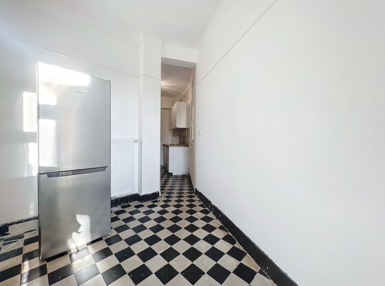 Cuisine minimaliste avec sol checkered noir et blanc, réfrigérateur argenté et espace lumineux.