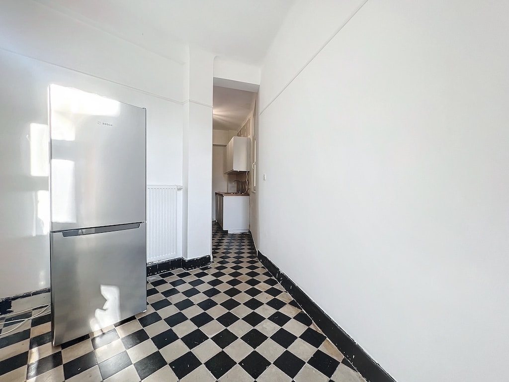 Cuisine minimaliste avec sol checkered noir et blanc, réfrigérateur argenté et espace lumineux.