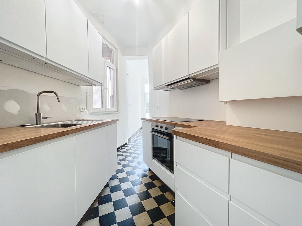 Cuisine moderne minimaliste avec armoires blanches, plan en bois chaud, sol rétro noir et blanc
