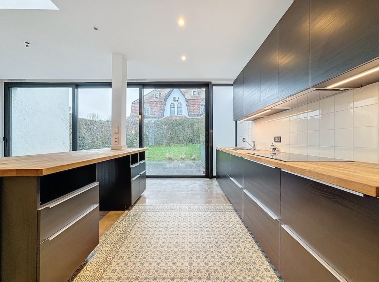 Cuisine moderne sombre avec plans en bois, grande baie vitrée et sol en carreaux élégants.