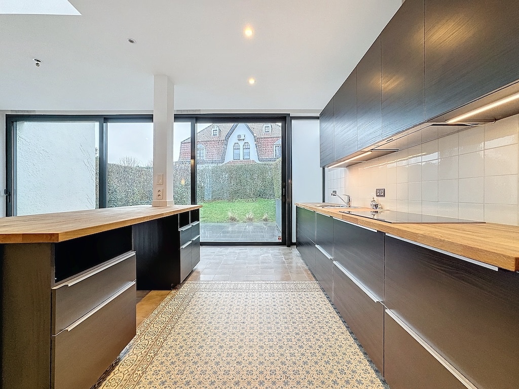 Cuisine moderne sombre avec plans en bois, grande baie vitrée et sol en carreaux élégants.