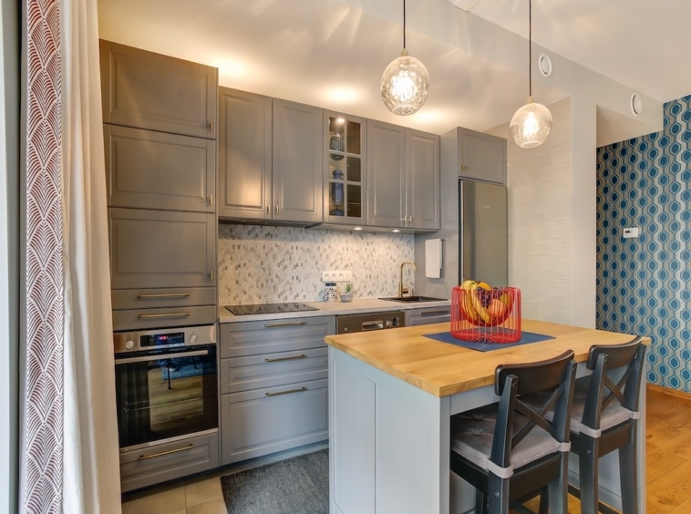 Cuisine moderne avec îlot en bois, meubles gris clair, éclairage élégant et mur bleu dynamisant.