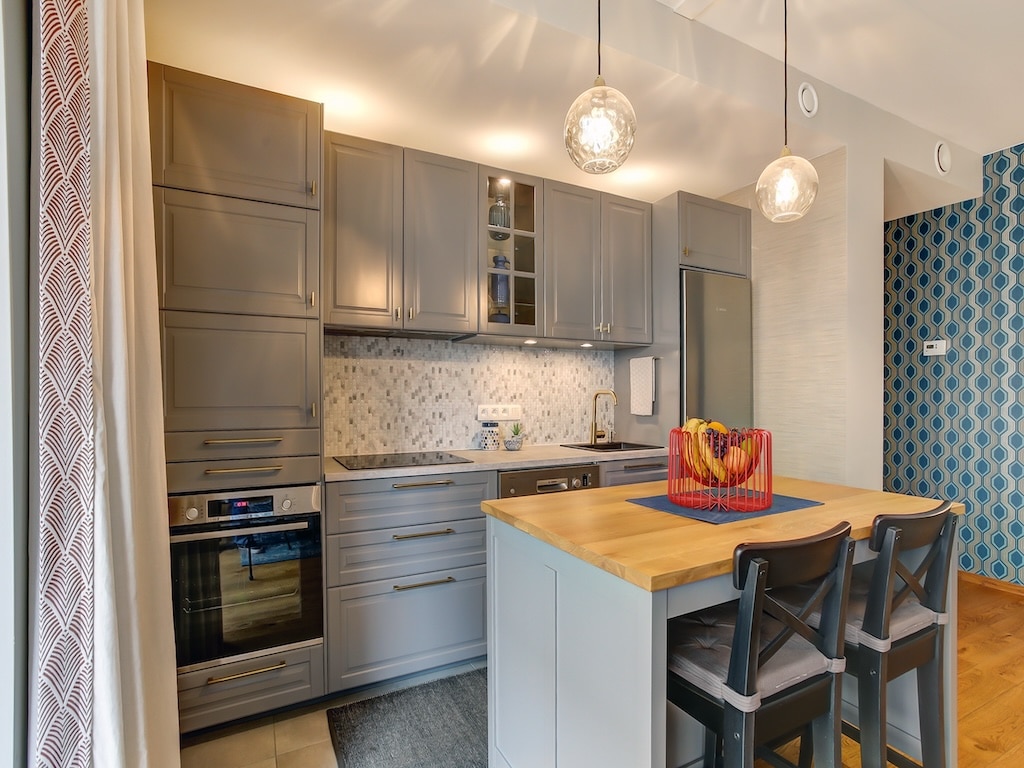 Cuisine moderne avec îlot en bois, meubles gris clair, éclairage élégant et mur bleu dynamisant.