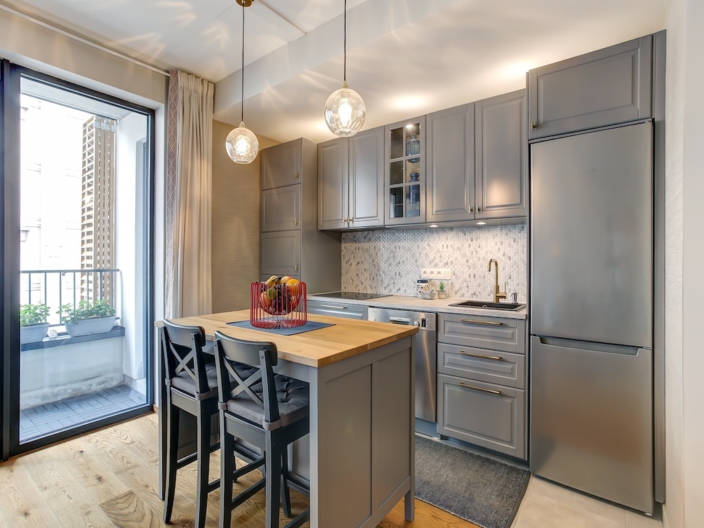 Cuisine moderne, lumineuse avec îlot en bois, meubles gris, électroménagers en acier et balcon.