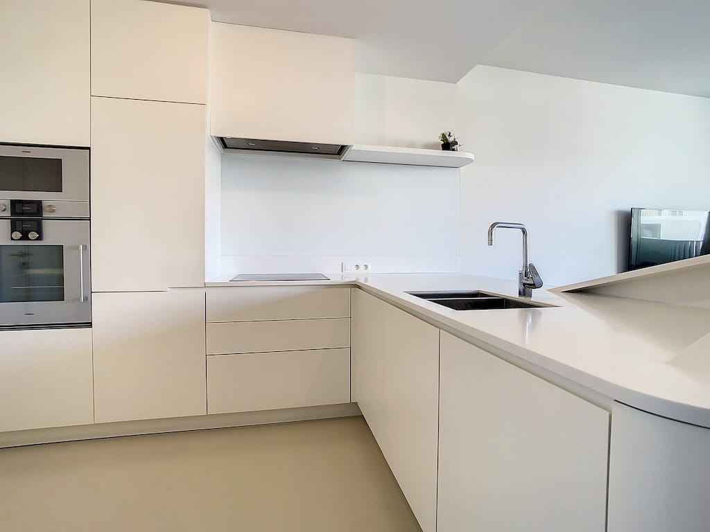 Cuisine moderne blanche, lumineuse, minimaliste, plans intégrés, appareils encastrés, design épuré.