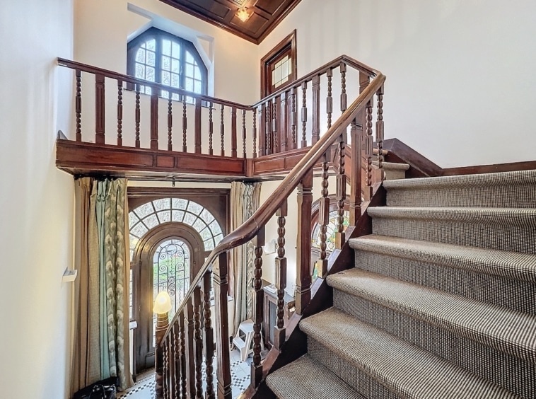 Foyer élégant avec escalier en bois, grande fenêtre arquée et décoration raffinée.