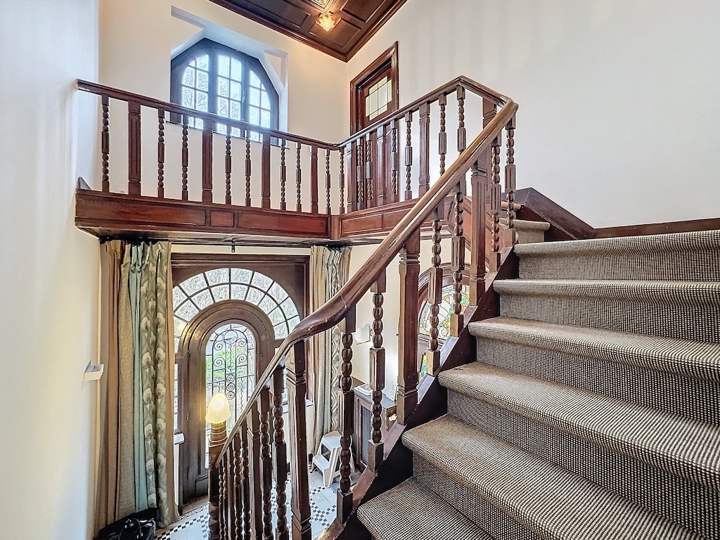 Foyer élégant avec escalier en bois, grande fenêtre arquée et décoration raffinée.