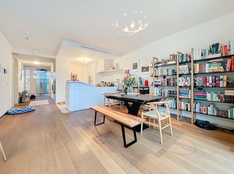 Salon lumineux avec cuisine ouverte, bibliothèque colorée, mobilier chaleureux et ambiance conviviale.