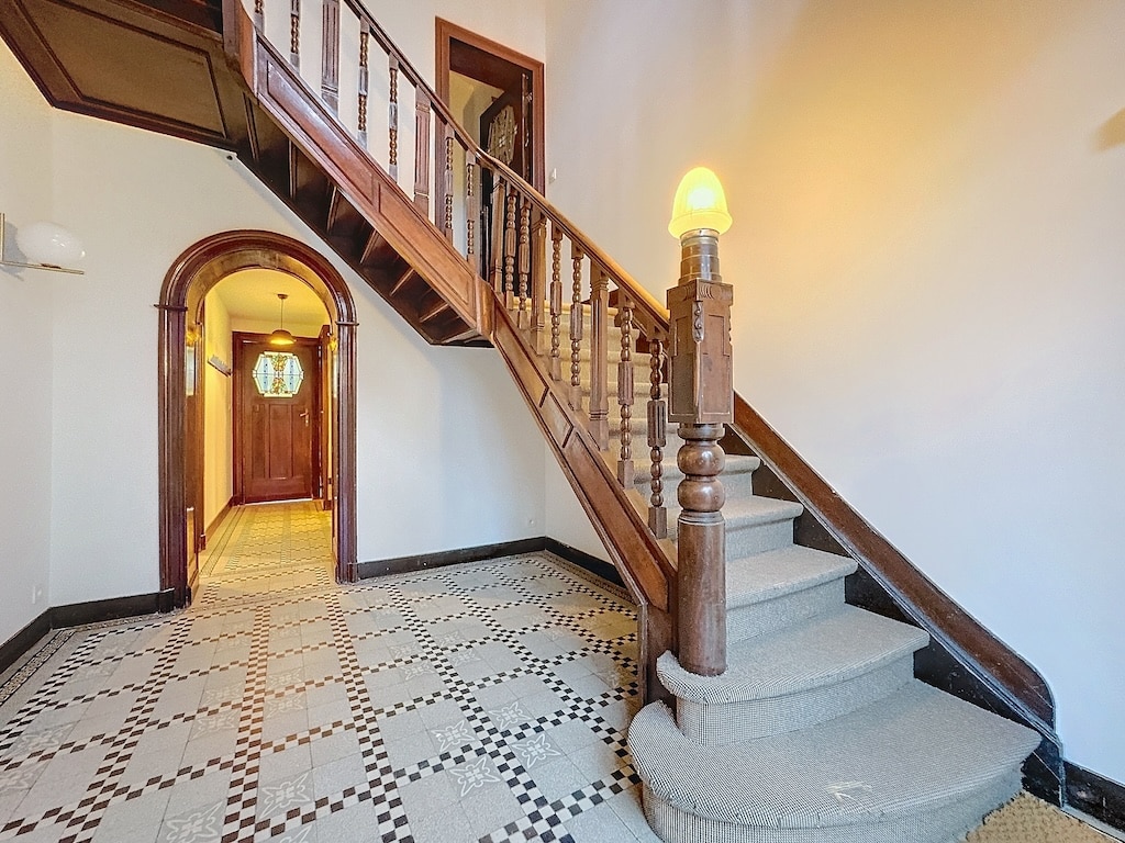 Hall d’entrée élégant avec escalier en bois, carrelage classique et ambiance chaleureuse.