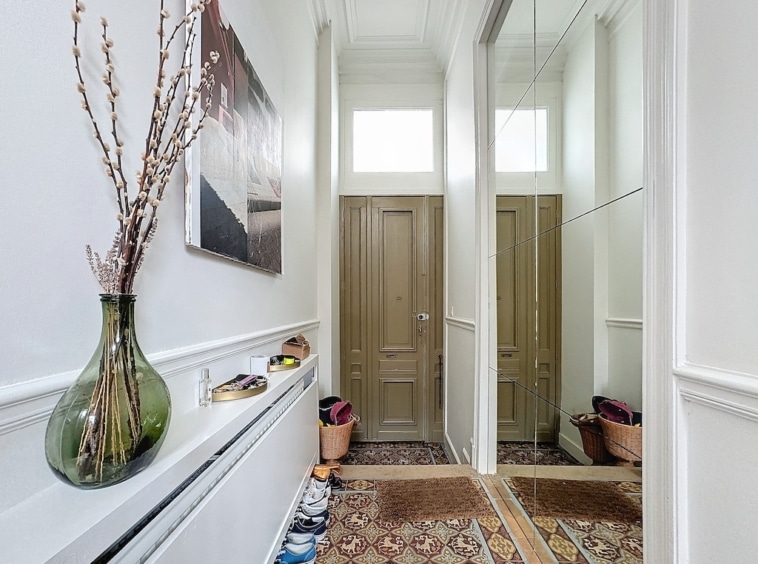 Couloir lumineux, élégant, avec miroirs, portes vert olive, tapis terreux, et décoration naturelle.