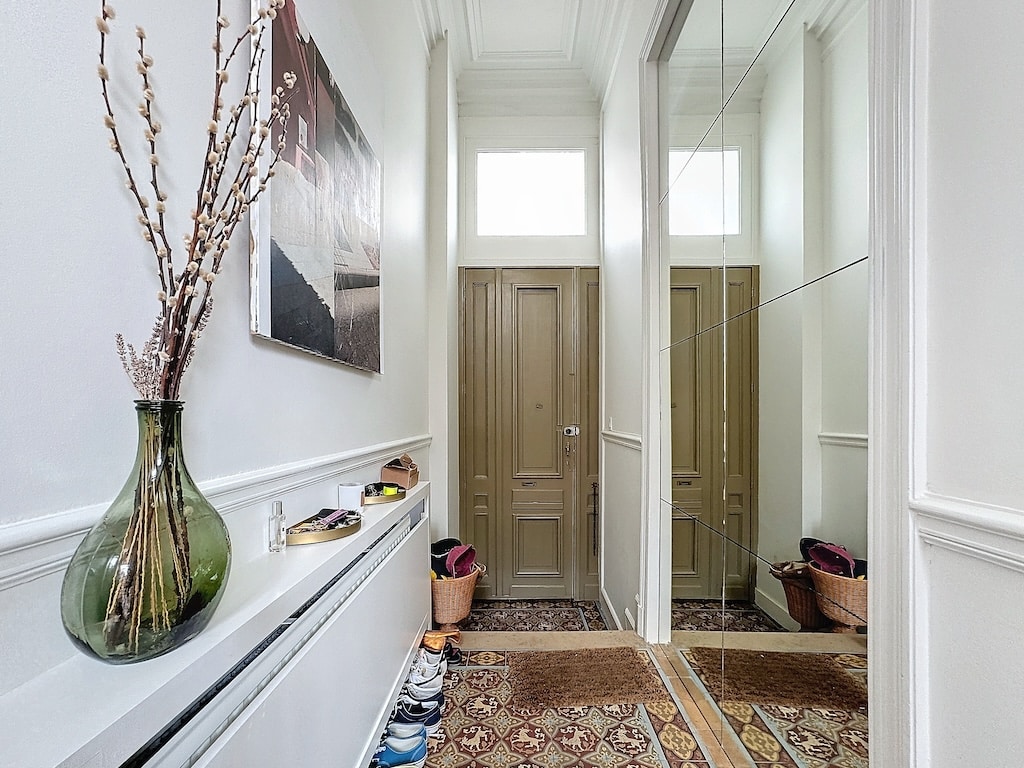Couloir lumineux, élégant, avec miroirs, portes vert olive, tapis terreux, et décoration naturelle.
