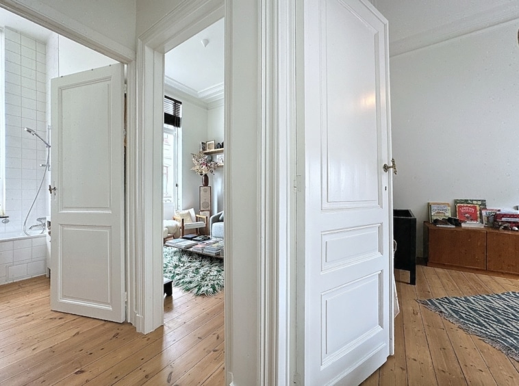 Couloir lumineux moderne avec sol en bois, murs blancs, espace de vie accueillant, ambiance chaleureuse.