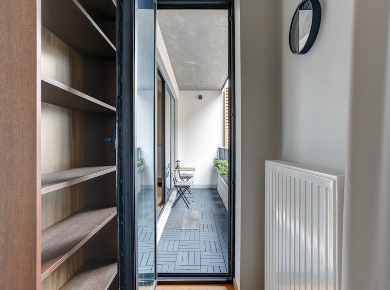 Couloir moderne lumineux avec balcon, plantes, mobilier en métal et décoration minimaliste.