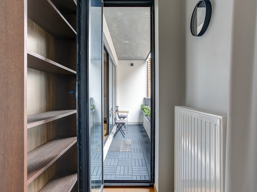 Couloir moderne lumineux avec balcon, plantes, mobilier en métal et décoration minimaliste.