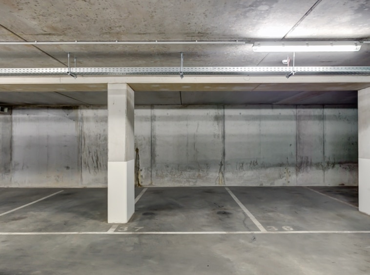 Parking souterrain urbain, espace vide, murs en béton, éclairage fluorescent, structure fonctionnelle.