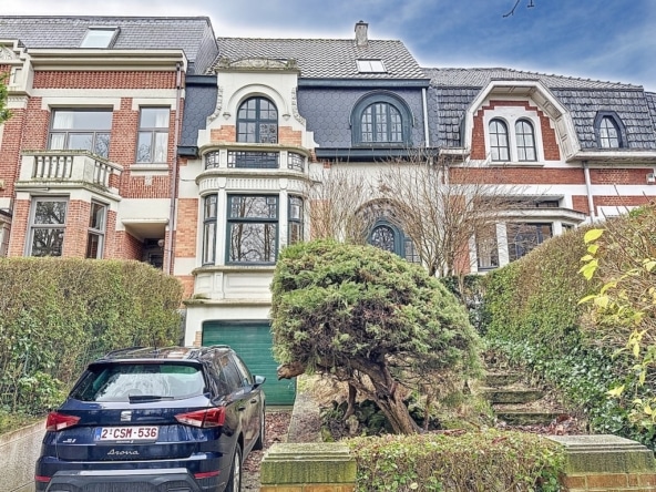 Villa historique avec jardin, fenêtres ornées, toit en tuiles, voiture moderne noire en avant.