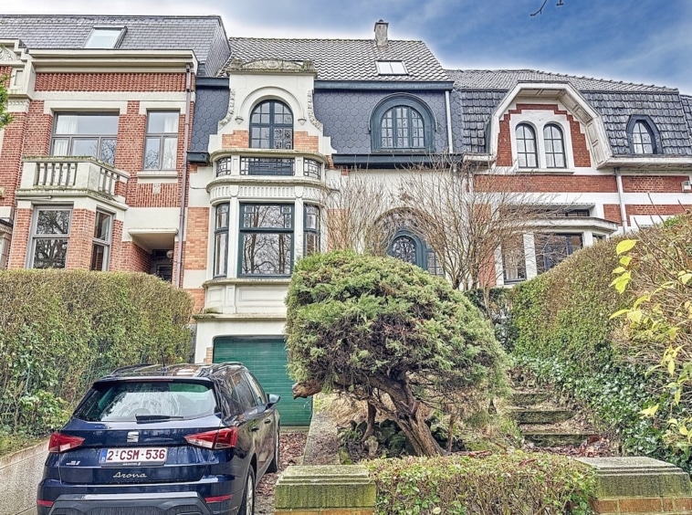 Villa historique avec jardin, fenêtres ornées, toit en tuiles, voiture moderne noire en avant.