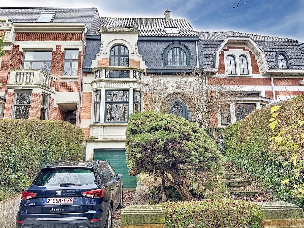 Villa historique avec jardin, fenêtres ornées, toit en tuiles, voiture moderne noire en avant.