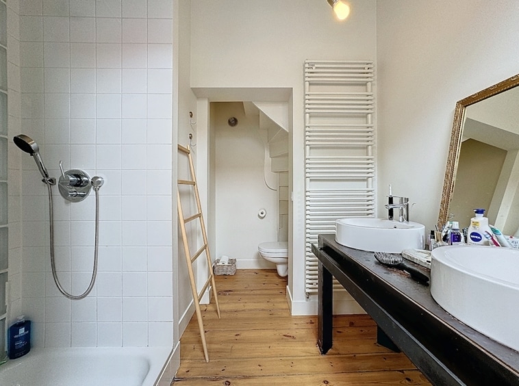 Salle de bain moderne avec lavabo rond en bois, douche en verre et touche rustique élégante.