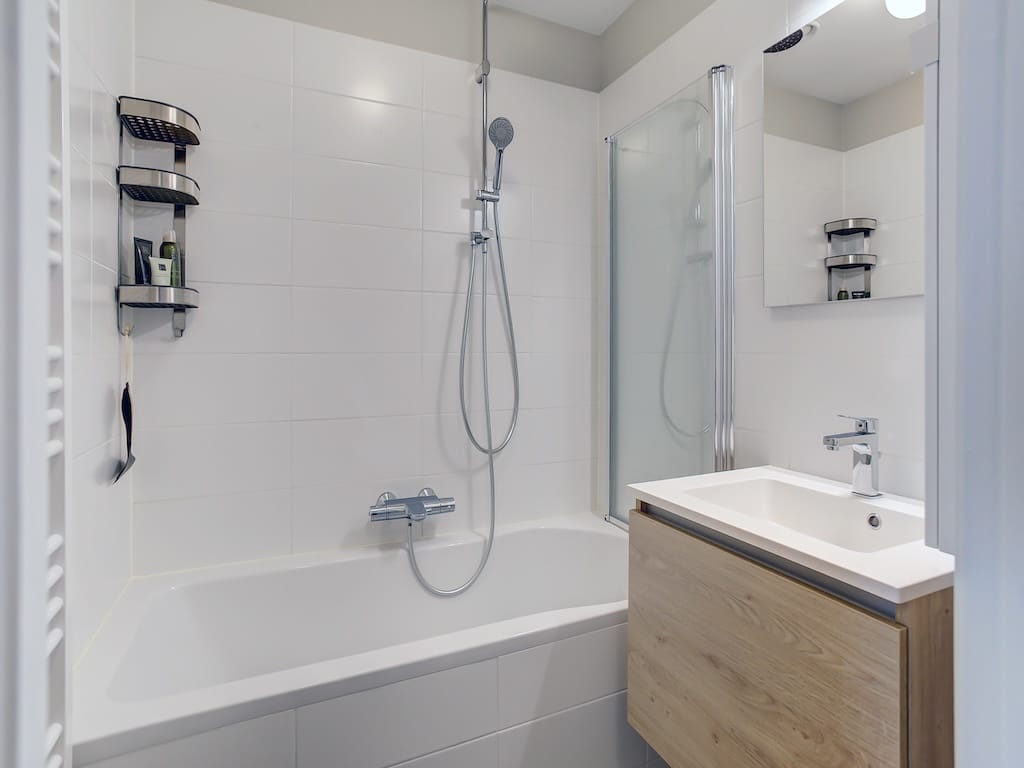 Salle de bain moderne, lumineuse, avec baignoire, douche à litalienne, miroir grand, rangements élégants.