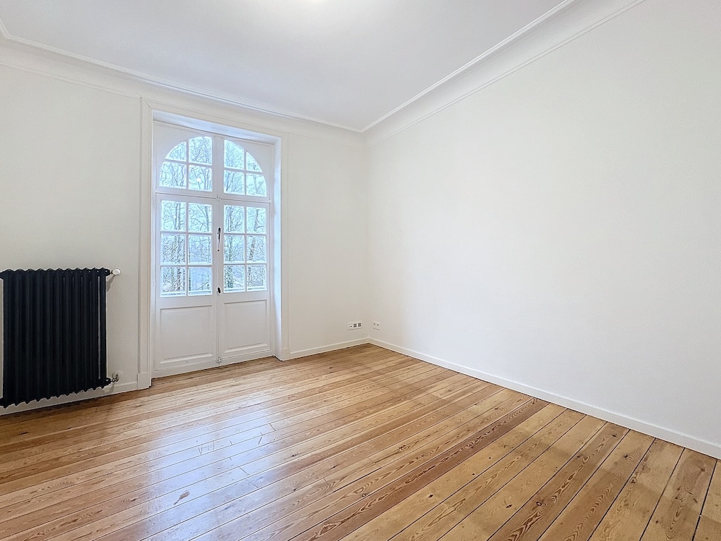 Salle vide minimaliste lumineuse avec parquet en bois clair et radiateur noir charme classique.