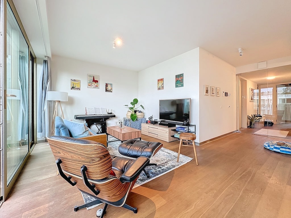 Salon moderne lumineux avec mobilier en bois, plantes, grand espace et accès balcon.