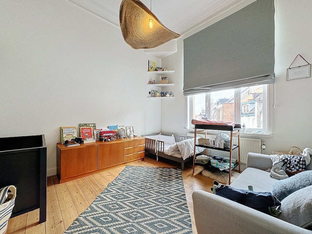 Salon minimaliste avec coin bébé, mobilier en bois, éclairage chaleureux, ambiance cosy et apaisante.