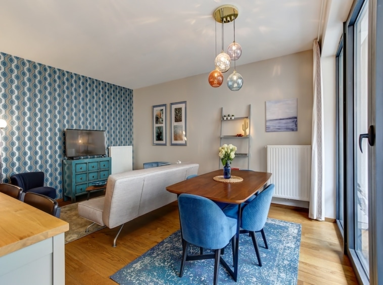 Salon moderne lumineux avec espace repas, fauteuils bleus, luminaire coloré, grande baie vitrée.
