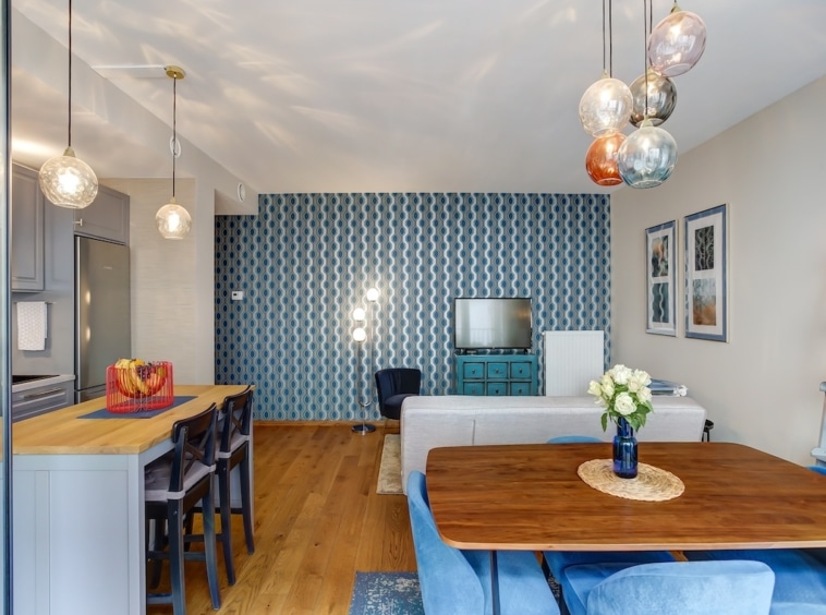Salon moderne avec cuisine ouverte, mur bleu géométrique, mobilier tendance et ambiance chaleureuse.
