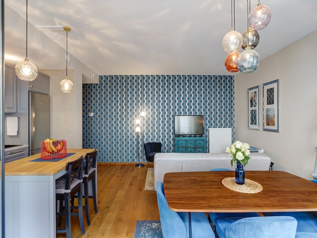 Salon moderne avec cuisine ouverte, mur bleu géométrique, mobilier tendance et ambiance chaleureuse.