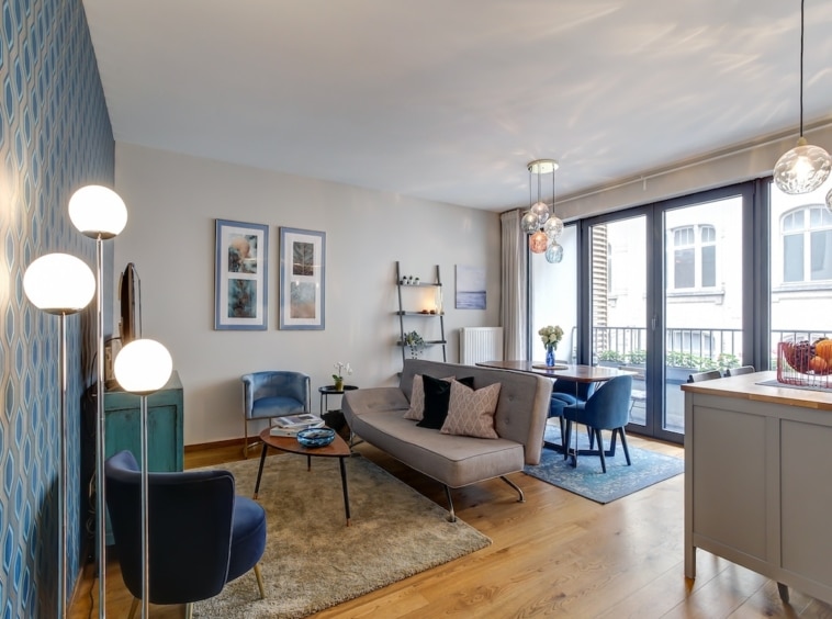 Salon moderne avec canapé gris, touches de bleu, lumière naturelle et déco élégante.