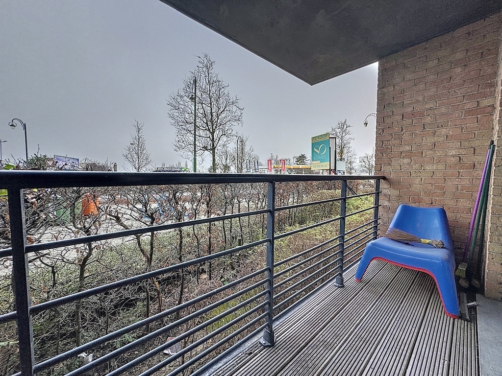Balcon moderne avec chaise colorée, vue urbaine et arbres dénudés en hiver sous ciel brumeux.