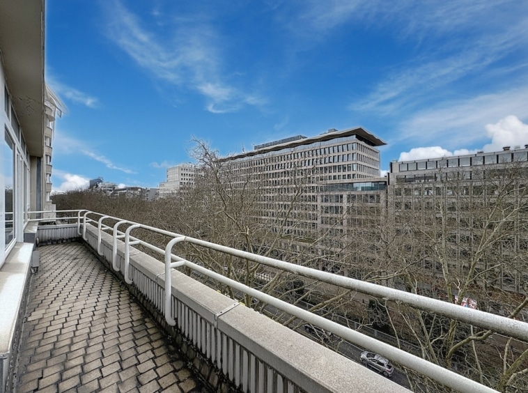 Balcon urbain moderne avec bâtiments en verre, arbres nus, ciel bleu et ambiance de tranquillité.
