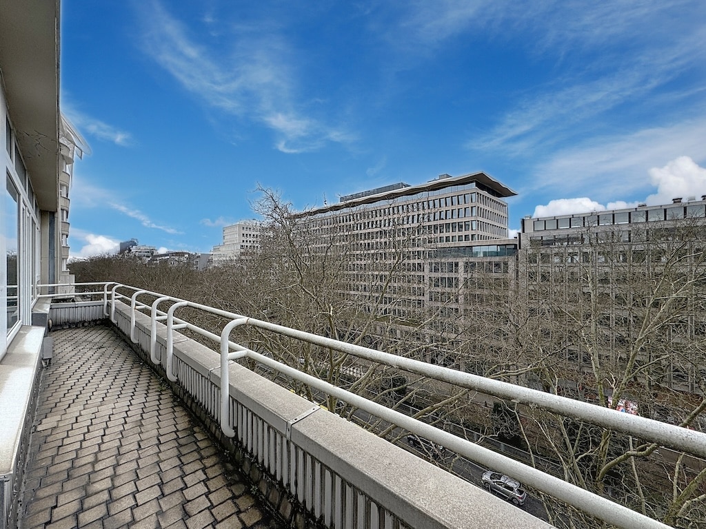 Balcon urbain moderne avec bâtiments en verre, arbres nus, ciel bleu et ambiance de tranquillité.