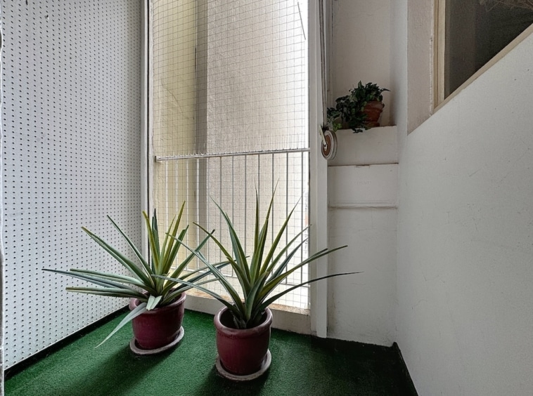 Balcon lumineux avec plantes vertes, faux gazon, grande fenêtre et ambiance apaisante.