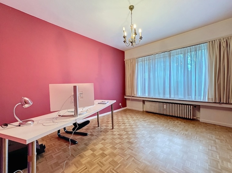 Bureau moderne avec mur rose vif, lumière naturelle, parquet en bois et ambiance chaleureuse.