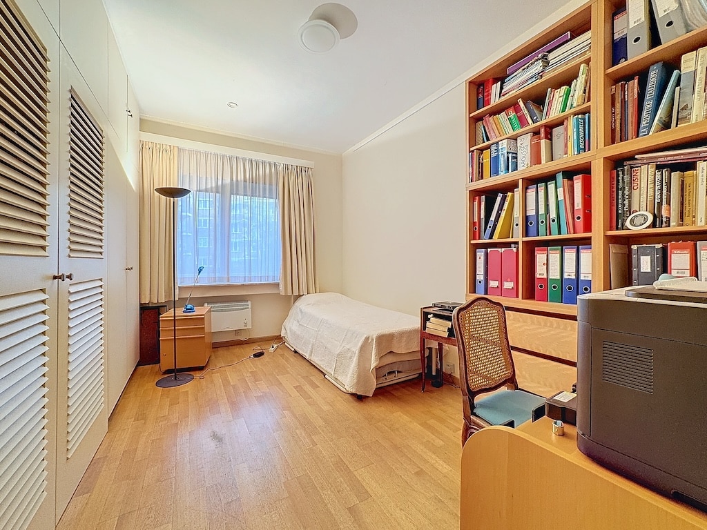 Chambre moderne et chaleureuse avec bibliothèque, bureau et luminosité naturelle, idéale pour détente et travail.