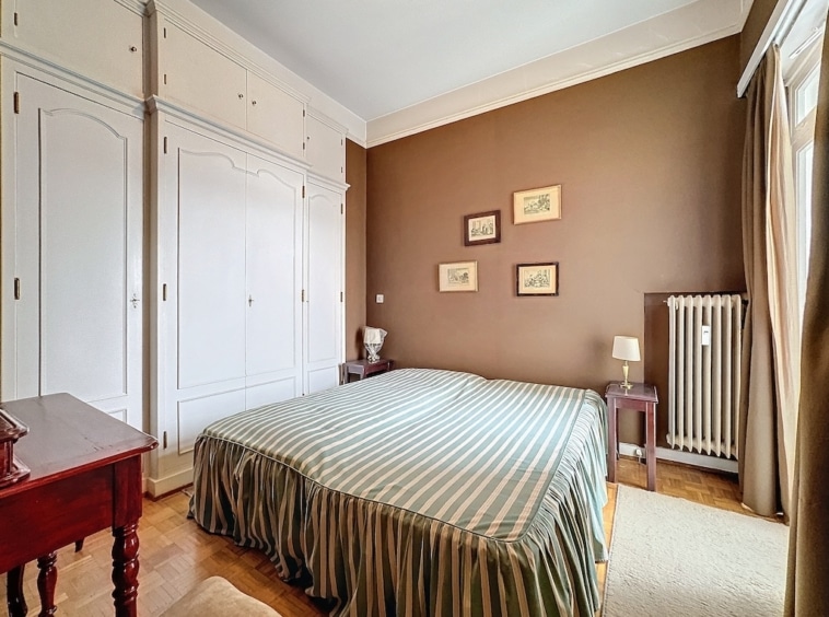 Chambre chaleureuse avec murs marron, lit rayé vert blanc, déco élégante et lumière naturelle.