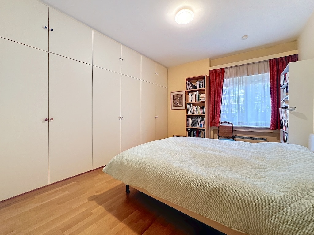 Chambre moderne et chaleureuse avec rangement épuré, fenêtre avec rideaux bordeaux, espace détente.