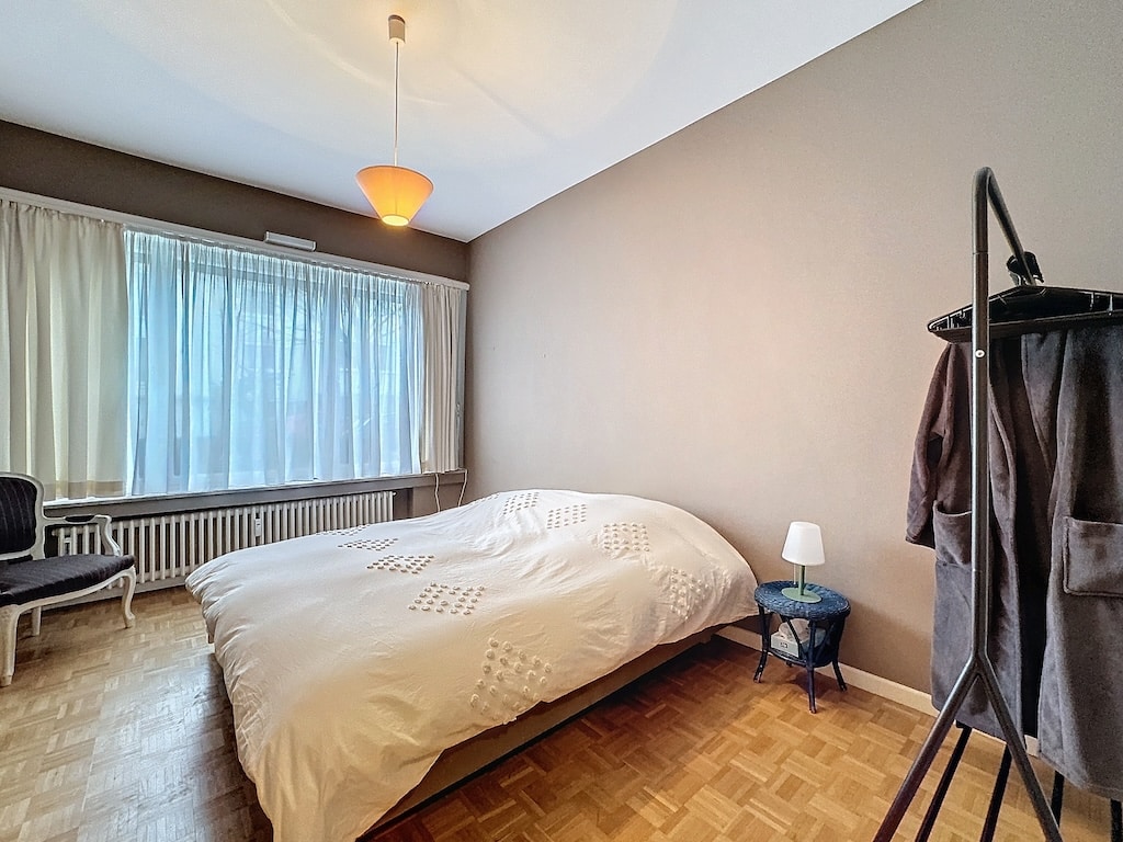Chambre lumineuse et minimaliste avec lit blanc, parquet, lumière naturelle et mobilier cosy.