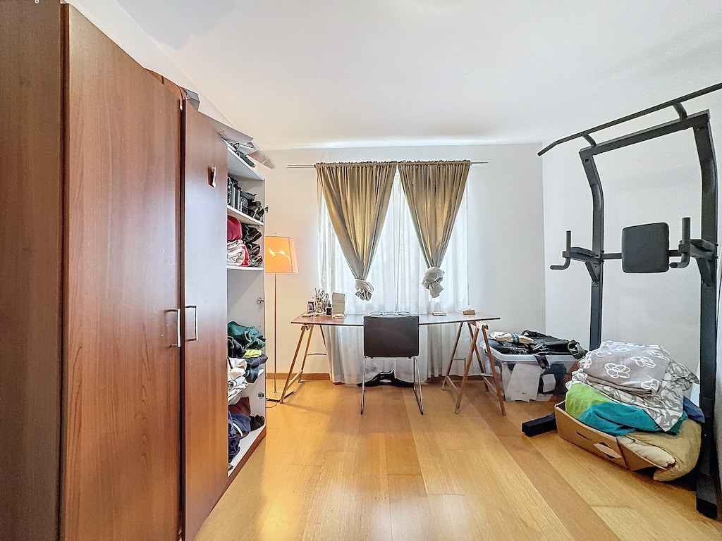 Chambre multifonctionnelle chaleureuse avec bureau, armoire, matériel de fitness et ambiance accueillante.