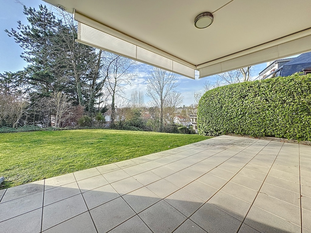 Terrasse ensoleillée avec gazon vert et haies, idéale pour détente en plein air.