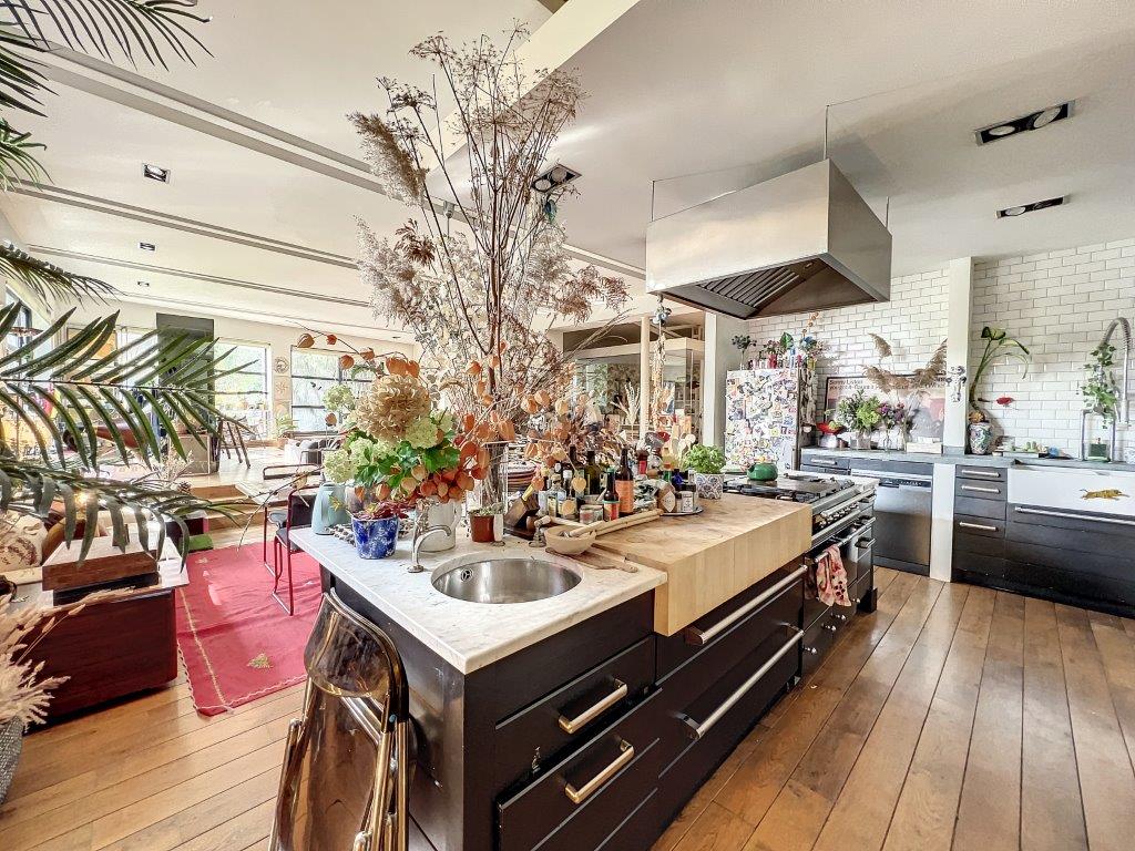 Cuisine moderne chaleureuse avec îlot en bois, plantes vertes et lumière naturelle.